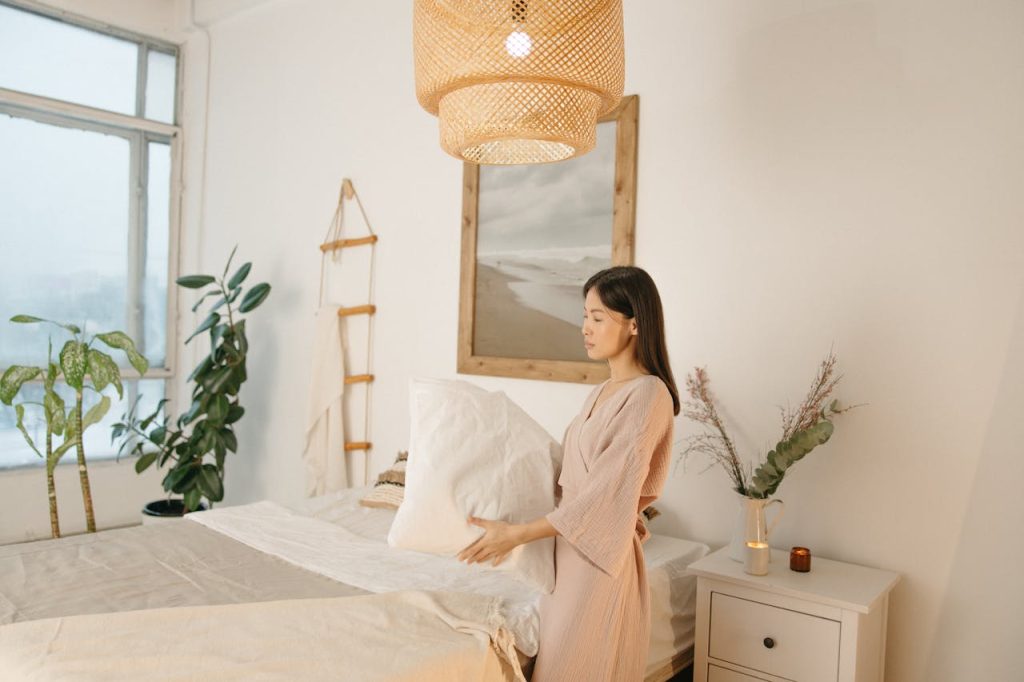 pexels photo 6792958 Asian woman arranging pillow in a cozy, minimalistic bedroom setting.