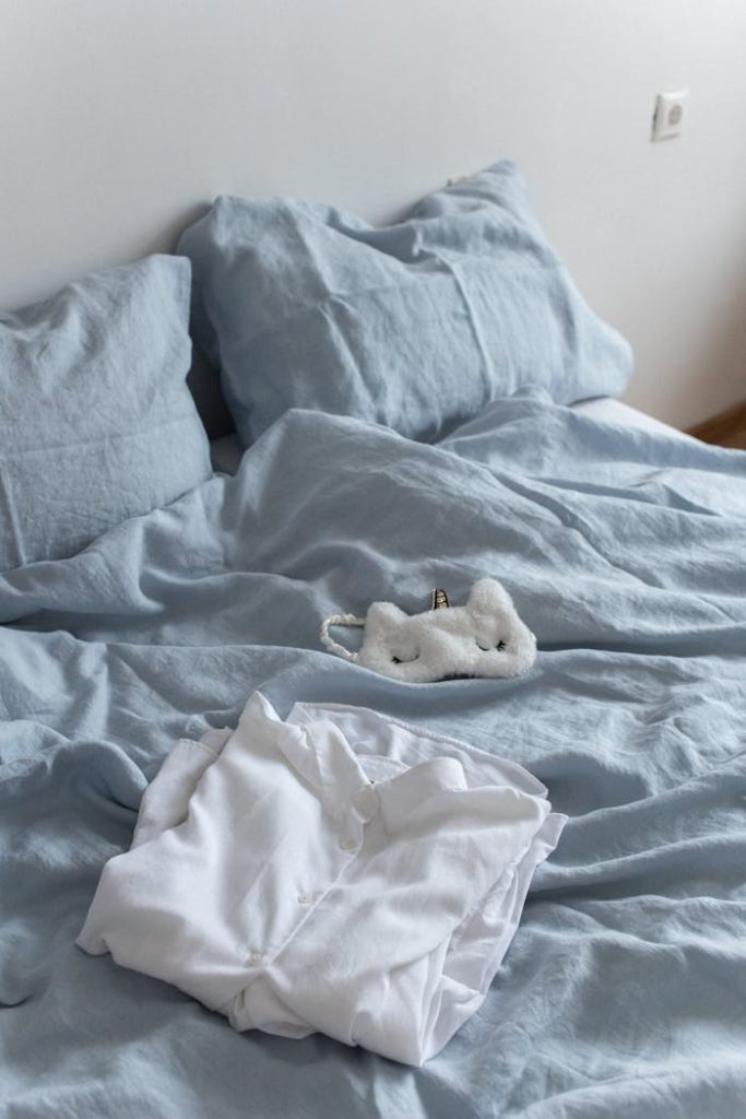 pexels photo 7445013 A cozy bedroom with light blue linen bedding and white pajamas, perfect for a relaxing atmosphere.